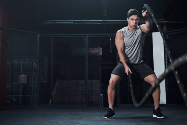 Shot of a young man working out with battle ropes at a gym